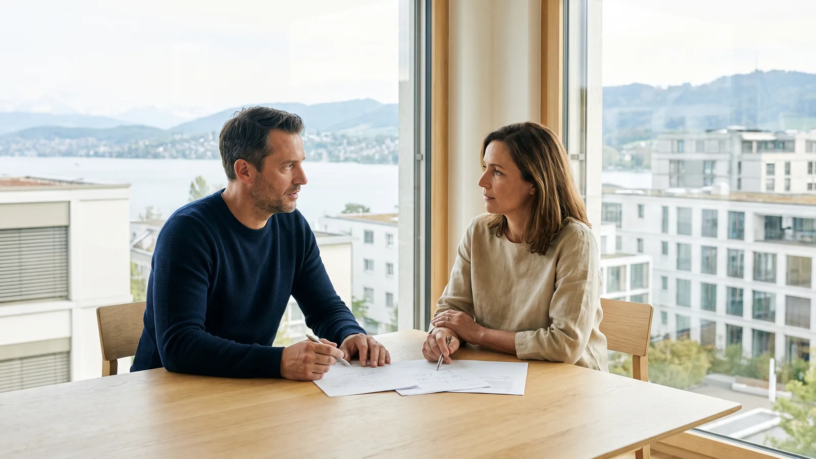Berater bespricht mit einer Kundin Unterlagen an einem hellen Besprechungstisch mit Blick auf den Zürichsee